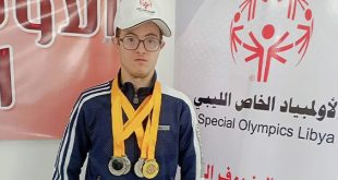 السباح عبد الهادي الرطيب يرتدي عدة ميداليات رياضية أمام لوحة تحمل شعار الأولمبياد الخاص الليبي.