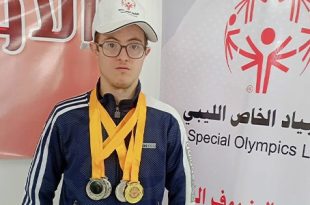 السباح عبد الهادي الرطيب يرتدي عدة ميداليات رياضية أمام لوحة تحمل شعار الأولمبياد الخاص الليبي.
