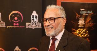 صورة للفنان سالم عيسى مبتسماً يظهر خلفه لافتة تحمل شعار "منتدى بنغازي للمسرح الكوميدي 2024