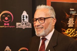 صورة للفنان سالم عيسى مبتسماً يظهر خلفه لافتة تحمل شعار "منتدى بنغازي للمسرح الكوميدي 2024