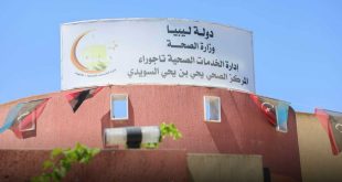 صورة لافتة بيضاء كبيرة تعتلي مبنى المركز الصحي يحيى بن يحيى السويدي في تاجوراء، مكتوب عليها "دولة ليبيا - وزارة الصحة - إدارة الخدمات الصحية تاجوراء - المركز الصحي يحيى بن يحيى السويدي"، ويظهر على جانبها شعار إدارة الخدمات الصحية، بينما تتدلى من المبنى أعلام ليبيا الصغيرة تحت سماء زرقاء صافية