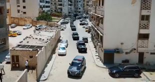 لقطة علوية تظهر رتلاً طويلًا من سيارات الدفع الرباعي والمدرعات السوداء والرمادية التابعة لإدارة إنفاذ القانون وهي تتحرك داخل شارع النصر السكني في طرابلس، وتحيط بها عمارات سكنية وسيارات مدنية متوقفة على جانبي الطريق