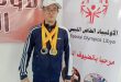 السباح عبد الهادي الرعيض يرتدي عدة ميداليات رياضية أمام لوحة تحمل شعار الأولمبياد الخاص الليبي.