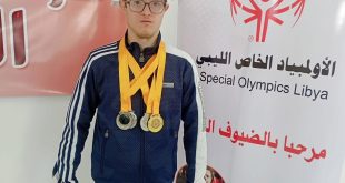 السباح عبد الهادي الرعيض يرتدي عدة ميداليات رياضية أمام لوحة تحمل شعار الأولمبياد الخاص الليبي.
