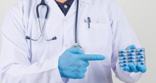 طبيب يرتدي معطفاً أبيض وقفازات طبية زرقاء ويشير بيده إلى شريط من كبسولات المضاد الحيوي.
