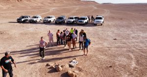 لقطة علوية واسعة من "عدسة الصباح" تُظهر فوجاً من السياح الأجانب والمحليين يقفون في منطقة صحراوية مفتوحة خارج مدينة غدامس التاريخية