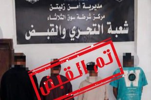 أربعة متهمين مغطى وجوههم يقفون أمام لافتة "مديرية أمن زليتن - مركز شرطة سوق الثلاثاء - شعبة التحري والقبض"،