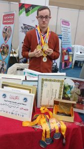 السباح عبد الهادي الرعيض يحمل ميداليات ذهبية أمام مجموعة من الشهادات والجوائز الرياضية خلال فعالية رياضية في ليبيا