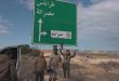 "عدة أشخاص يقفون بجوار لافتة طرق خضراء تشير إلى طرابلس ومصراتة وسرت، بالقرب من طريق في منطقة مفتوحة ذات طبيعة صحراوية"
