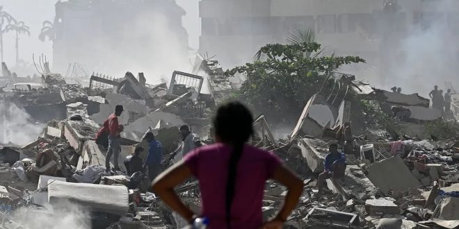​امرأة تنظر إلى ركام مبانٍ منهارة وأشخاص يبحثون بين الأنقاض وسط تصاعد الغبار بعد زلزال فنزويلا المدمر.
