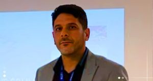 لقطة مقربة للدكتور حسن الجعفري، مدير إدارة الموانئ والمرافئ بوزارة الثروة البحرية الليبية، يرتدي بدلة رسمية ويتحدث في مناسبة رسمية وخلفه شاشة عرض بيضاء، مع وجود شعار منصة الصباح.