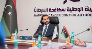 رئيس الهيئة الوطنية لمكافحة السرطان يجلس على رأس طاولة اجتماع بمقر الهيئة، وخلفه شعار الهيئة والعلم الليبي، خلال مناقشة ملف توفير أدوية الأورام والخدمات العلاجية.