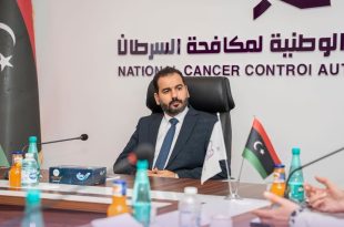 رئيس الهيئة الوطنية لمكافحة السرطان يجلس على رأس طاولة اجتماع بمقر الهيئة، وخلفه شعار الهيئة والعلم الليبي، خلال مناقشة ملف توفير أدوية الأورام والخدمات العلاجية.