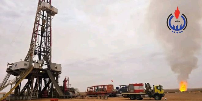 برج حفر ونفط ضخم تابع لشركة سرت لإنتاج وتصنيع النفط والغاز في حقل متخندوش بجانبه شاحنات ومعدات تشغيل، ويظهر في الخلفية شعلة غاز متصاعدة في السماء مع شعار المؤسسة الوطنية للنفط الليبية أعلى اليمين
