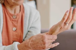 لقطة قريبة لامرأة مسنة تمسك بمعصم يدها وتبدو عليها علامات الألم أو الضعف في المفاصل والعظام،