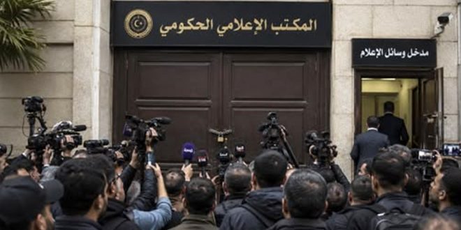 تجمع لعدد من الصحفيين والمصورين يحملون الكاميرات والميكروفونات أمام البوابة الرئيسية المغلقة لـ "المكتب الإعلامي الحكومي" المقفلة بقفل حديدي، وإلى جانبها ممر فرعي مفتوح تعلوه لافتة مكتوب عليها "مدخل وسائل الإعلام