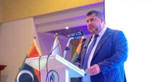 رئيس مجلس إدارة المؤسسة الوطنية للنفط مسعود سليمان يرتدي بدلة رسمية كحلية ويقف خلف منصة تتضمن شعار المؤسسة والعلم الليبي متحدثاً عبر الميكروفون في ورشة عمل حول تطوير صناعة الغاز الطبيعي