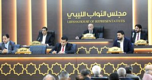 لقطة عامة من داخل قاعة مجلس النواب الليبي تُظهر رئيس المجلس المستشار عقيلة صالح جالساً في المنتصف وخلفه شعار "مجلس النواب الليبي، وبجانبه أعضاء هيئة الرئاسة والمقرر والمراقبون خلف منصة خشبية مزينة بزخارف إسلامية هندسية، وأمامهم يظهر جزء من الحضور والنائبين