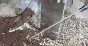 "لقطة قريبة تظهر جزءاً من آلة عجن صناعية داخل مخبز، حيث يختلط مسحوق داكن اللون يشبه الكاكاو مع الدقيق الأبيض والنخالة على أسطح الآلة المعدنية أثناء إعداد العجين."