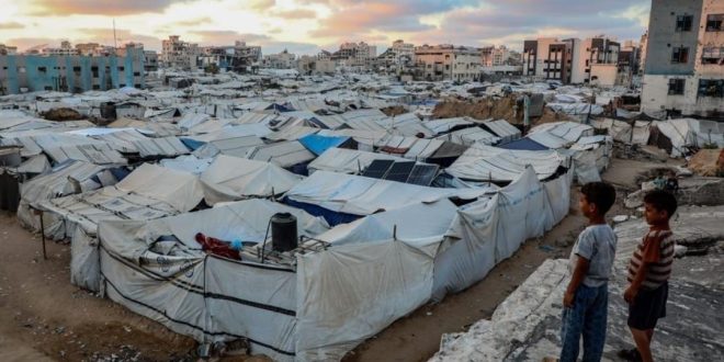 لقطة علوية لمخيم شاسع ومزدحم للنازحين في قطاع غزة، مليء بصفوف من الخيام القماشية والبلاستيكية البيضاء والرمادية المتهالكة،