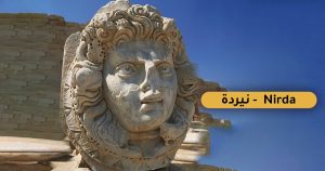 لقطة مقربة لمنحوتة رخامية بارزة تمثل رأس حورية البحر الأسطورية (النيردة) بملامح بارزة وشعر متموج يتداخل مع تفاصيل بحرية، وخلفها جدار أثري وسماء زرقاء، ويظهر في الجانب الأيمن ملصق توضيحي أصفر مكتوب عليه "نيردة