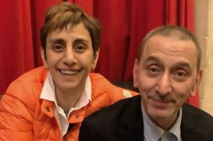 صورة تجمع المخرجة ريما الرحباني وشقيقها الفنان زياد الرحباني يبتسمان أمام خلفية ستارة حمراء.
