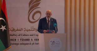 ​لقطة لوزير الثقافة والتنمية المعرفية الليبي مبروك توفي وهو يلقي كلمته خلف منصة تحمل شعار "موسم ليبيا الثقافي"، وبجانبه العلم الليبي وخلفية بشعار الوزارة باللغتين العربية والأمازيغية
