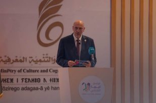 ​لقطة لوزير الثقافة والتنمية المعرفية الليبي مبروك توفي وهو يلقي كلمته خلف منصة تحمل شعار "موسم ليبيا الثقافي"، وبجانبه العلم الليبي وخلفية بشعار الوزارة باللغتين العربية والأمازيغية
