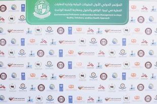 ​لوحة خلفية بيضاء كبيرة خاصة بالملتقى البيئي الأول في طرابلس، يظهر في أعلاها لافتة خضراء مكتوب عليها باللغتين العربية والإنجليزية "المؤتمر الدولي الأول لإدارة الملوثات البيئية والنفايات الخطرة في ليبيا"، وتتكرر على بقية اللوحة شعارات الجهات المشاركة والمنظمة بشكل منتظم.