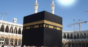 ​لقطة مهيبة للكعبة المشرفة بكسوتها السوداء المطرزة بالآيات القرآنية الذهبية وسط صحن المطاف بالمسجد الحرام في مكة المكرمة، وتظهر مئذنتان من مآذن الحرم الشريف خلفها، مع قرص الشمس الساطع والمتوهج في سماء زرقاء صافية أعلى الكعبة مباشرة في لحظة التعامد