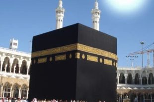 ​لقطة مهيبة للكعبة المشرفة بكسوتها السوداء المطرزة بالآيات القرآنية الذهبية وسط صحن المطاف بالمسجد الحرام في مكة المكرمة، وتظهر مئذنتان من مآذن الحرم الشريف خلفها، مع قرص الشمس الساطع والمتوهج في سماء زرقاء صافية أعلى الكعبة مباشرة في لحظة التعامد