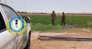 ​جانب من سيارة دورية تابعة لجهاز الشرطة الزراعية الليبية يظهر عليها شعار وزارة الزراعة والثروة الحيوانية، وفي الخلفية يظهر عنصران من أفراد الأمن يرتديان الزي العسكري أثناء قيامهما بجولة تفتيشية داخل حقل زراعي أخضر في منطقة قصر بن غشير