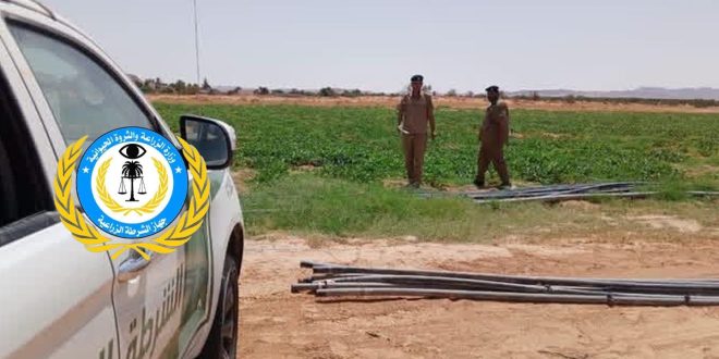 ​جانب من سيارة دورية تابعة لجهاز الشرطة الزراعية الليبية يظهر عليها شعار وزارة الزراعة والثروة الحيوانية، وفي الخلفية يظهر عنصران من أفراد الأمن يرتديان الزي العسكري أثناء قيامهما بجولة تفتيشية داخل حقل زراعي أخضر في منطقة قصر بن غشير