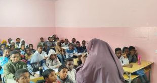 مجموعة من الأطفال والطلاب اللاجئين والمهاجرين من ذوي البشرة السمراء يجلسون على مقاعدهم الدراسية باهتمام، بينما تقف معملة ترتدي حجاباً تلتف بظهرها نحو الكاميرا لتشرح لهم الدرس