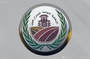 ​شعار دائري رسمي لـ "النقابة العامة للمزارعين"، يتضمن رسمًا لجرار زراعي باللون الأسود في المنتصف وحقولًا ملونة في الأسفل، يحيط به غصنان من أوراق الشجر الخضراء، على خلفية رمادية ذات تأثيرات رقمية خفيفة