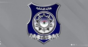 ​"شعار رسمي لوزارة الداخلية والشرطة الليبية يأتي على شكل درع باللون الأزرق الداكن والإطار الفضي، مكتوب في أعلاه 'وزارة الداخلية' وفي أسفله 'الشرطة'، ويتوسطه رمز نجمة وإكليل وشعار العين بألوان العلم الليبي، بخلفية رمادية."