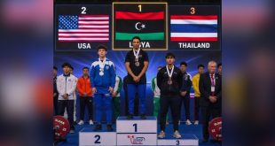 البطل الليبي محمد الساحلي يقف على منصة التتويج بالمركز الأول رافعًا علم ليبيا، وبجانبه الفائزان بالمركزين الثاني والثالث من الولايات المتحدة وتايلاند.
