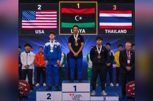البطل الليبي محمد الساحلي يقف على منصة التتويج بالمركز الأول رافعًا علم ليبيا، وبجانبه الفائزان بالمركزين الثاني والثالث من الولايات المتحدة وتايلاند.