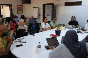مجموعة من الصحفيين والإعلاميين الليبيين يشاركون في حلقة نقاشية أو ورشة عمل داخل قاعة اجتماعات، حيث يلتفون حول طاولة بيضاء كبيرة ويستمعون بتركيز لأحد المتحدثين، في بيئة عمل مهنية تجسد النقاشات حول واقع الصحافة والإعلام