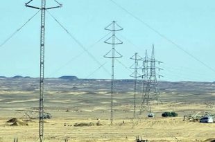 لقطة نهارية تظهر عدة أبراج وخطوط لنقل الطاقة الكهربائية ممتدة عبر منطقة صحراوية مفتوحة، مع وجود بعض الآليات وسيارات العمل الفنية في الموقع لاستكمال المشروعات المعتمدة للشركة العامة للكهرباء. خط قمرا (2)