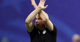 لقطة للمدير الفني لمنتخب مصر يرفع ذراعيه متقاطعتين على شكل حرف X (إشارة مكافحة العنصرية) أثناء مباراة، مرتدياً قميصاً أسود يحمل شعار المنتخب، والخلفية زرقاء.