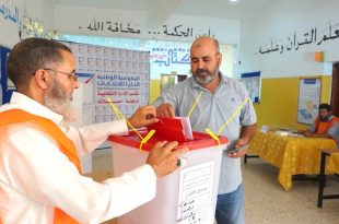 أحد الناخبين يدلي بصوته في صندوق الاقتراع داخل مركز انتخابي، بحضور موظف تابع للمفوضية الوطنية العليا للانتخابات يشرف على سير العملية الانتخابية.