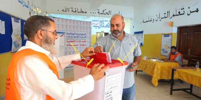 أحد الناخبين يدلي بصوته في صندوق الاقتراع داخل مركز انتخابي، بحضور موظف تابع للمفوضية الوطنية العليا للانتخابات يشرف على سير العملية الانتخابية.