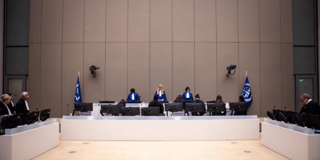 قاعة محكمة حديثة تضم ثلاثة قضاة على المنصة الرئيسية، مع محامين وممثلي الأطراف يجلسون أمام شاشات الحاسوب داخل جلسة قضائية رسمية، وتظهر أعلام المحكمة على جانبي المنصة