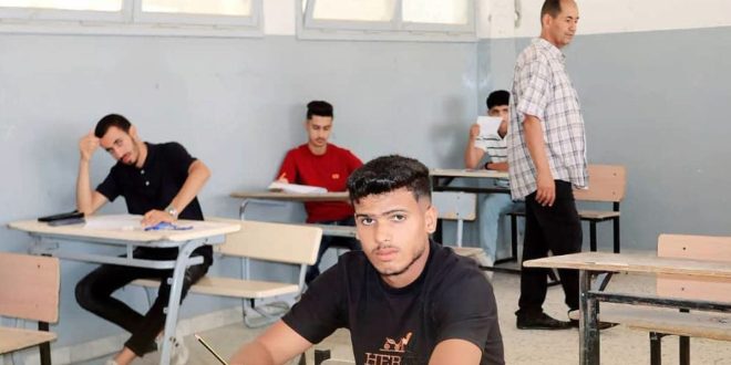 طلاب يؤدون امتحان الدور الثاني للشهادة الثانوية داخل قاعة امتحان، بينما يشرف أحد المراقبين على سير الامتحانات.