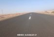لقطة واسعة ممتدة تظهر مسار طريق إسفلتي حديث ممتد وسط بيئة صحراوية في الجنوب الليبي،