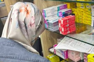 مفتشة من فريق الإصحاح البيئي ترتدي حجابًا منقوشًا وجاكيت جينز تفحص أرفف الأدوية والعلب الطبية داخل إحدى الصيدليات أثناء جولة تفتيشية
