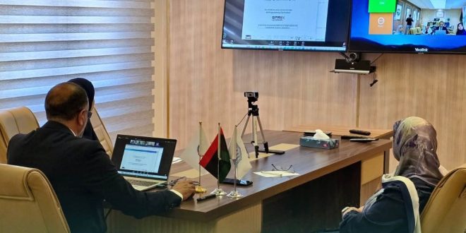 أمين عام اللجنة الوطنية للتربية والثقافة والعلوم حسين المشرقي ومسؤولون يجلسون حول طاولة اجتماعات بها أعلام صغيرة