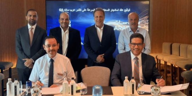 صورة لمراسم توقيع اتفاقية بين مسئولين من شركة ليبيا للاتصالات والتقنية "LTT" والمنظمة العربية للاتصالات الفضائية "عرب سات"، حيث يجلس شخصان على طاولة توقيع العقود وأمامهما المستندات، وخلفهما أربعة من المسئولين يقفون أمام شاشة عرض مكتوب عليها "توقيع عقد استئجار السعات... على القمر عرب سات 6A".