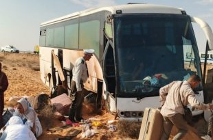 حافلة سياحية بيضاء متضررة إثر خروجها عن الطريق الصحراوي في منطقة النفاتية باتجاه بن قردان، وركاب وعناصر أمن وإنقاذ يقفون بجوار الحافلة بين الأمتعة على جانب الطريق